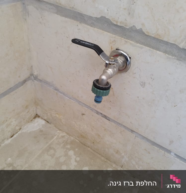 ברז מתכת עם ידית שחורה על קיר